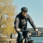 Mann som sykler langs elva en solfylt vårdag.